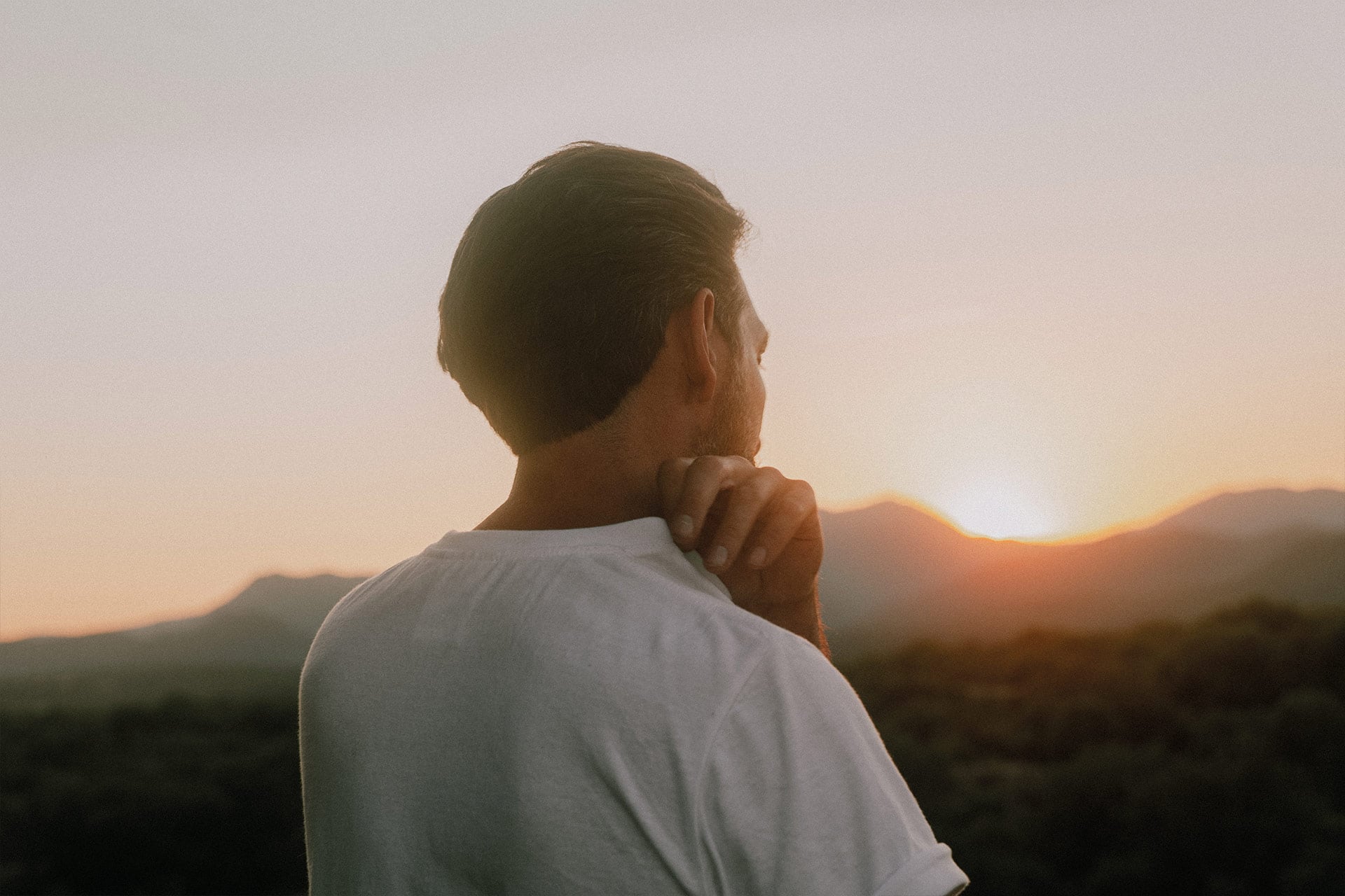 Un homme de dos au couch&eacute; du soleil porte un t-shirt et touche son &eacute;paisseur